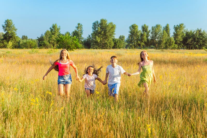 Vier glückliche schöne Kinder, die am schönen Sommertag zusammenrücken spielend laufen stockbild Vier glückliche schöne Kinder, die am schönen Sommertag zusammenrücken spielend laufen stockbild