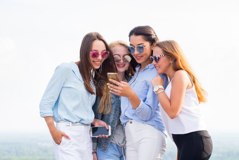 Vier jonge vrouwen in zonnebril gebruiken smartphone zich bevindt op het dak van het gebouw Vriendschap en moderne technologiecon stock foto's Vier jonge vrouwen in zonnebril gebruiken smartphone zich bevindt op het dak van het gebouw Vriendschap en moderne technologiecon stock foto's