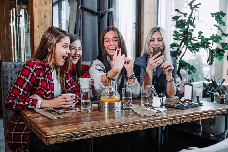 Vier junge Frauen, die im Café unter Verwendung des intelligenten Telefons sitzen und lustiges Gespräch haben stockfotografie Vier junge Frauen, die im Café unter Verwendung des intelligenten Telefons sitzen und lustiges Gespräch haben stockfotografie