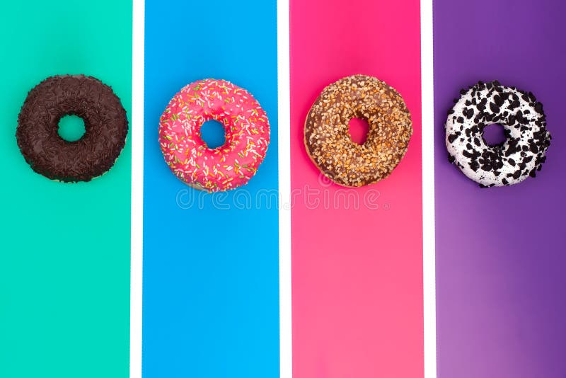 Four different donuts chokolate, nuts, fruit pink, milk creamy on bright multicolored top view close up. Four different donuts chokolate, nuts, fruit pink, milk creamy on bright multicolored top view close up