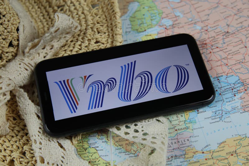 Closeup of mobile phone screen wit logo lettering of online booking travel agency vrbo with sun hat and map