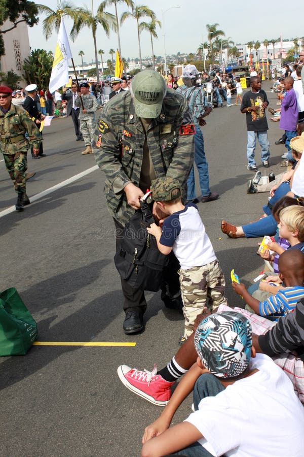 A Vietnam Veteran allows a boy wearing Army pants and hat dig into his bag of patriotic items. This symbolic gesture was captured as spectators crowded the streets of downtown San Diego to witness this year's Annual Veterans' Day parade. This annual event attracts thousands of participants from all branches of the military. The parade was participated by veterans, their families and students of all ages, most aspiring to be a member of the US Armed Forces themselves. Veterans' Day is celebrated in the United States in honor of those who made the ultimate sacrifice for the freedom of the country. A Vietnam Veteran allows a boy wearing Army pants and hat dig into his bag of patriotic items. This symbolic gesture was captured as spectators crowded the streets of downtown San Diego to witness this year's Annual Veterans' Day parade. This annual event attracts thousands of participants from all branches of the military. The parade was participated by veterans, their families and students of all ages, most aspiring to be a member of the US Armed Forces themselves. Veterans' Day is celebrated in the United States in honor of those who made the ultimate sacrifice for the freedom of the country.