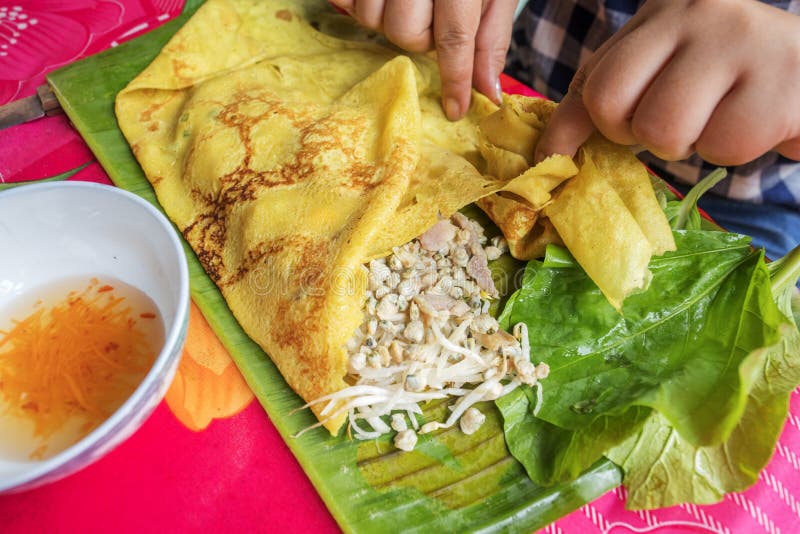 Wrapping crispy Vietnamese crepe (Banh Xeo) with vegetables, Ben Tre Province, Vietnam. Banh Xeo , literally sizzling cake, named for the loud sizzling sound it makes when the rice batter is poured into the hot skillet is a Vietnamese savory fried pancake (it resembles a French crepe with a crispy edge) made of rice flour, water, turmeric powder, stuffed with slivers of fatty pork, shrimp, diced green onion, and bean sprouts. Báº¿n Tre is a province of Vietnam. It is one of the country's southern provinces, being situated in the Mekong Delta. Wrapping crispy Vietnamese crepe (Banh Xeo) with vegetables, Ben Tre Province, Vietnam. Banh Xeo , literally sizzling cake, named for the loud sizzling sound it makes when the rice batter is poured into the hot skillet is a Vietnamese savory fried pancake (it resembles a French crepe with a crispy edge) made of rice flour, water, turmeric powder, stuffed with slivers of fatty pork, shrimp, diced green onion, and bean sprouts. Báº¿n Tre is a province of Vietnam. It is one of the country's southern provinces, being situated in the Mekong Delta.