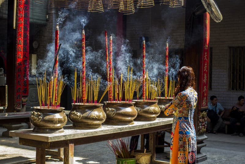 Vietnamesische Frau im Trachtenkleid AO Dai, das mit Räucherstäbchen im brennenden Topf der chinesischen Pagode in Ho Chi Minh be lizenzfreies stockbild Vietnamesische Frau im Trachtenkleid AO Dai, das mit Räucherstäbchen im brennenden Topf der chinesischen Pagode in Ho Chi Minh be lizenzfreies stockbild