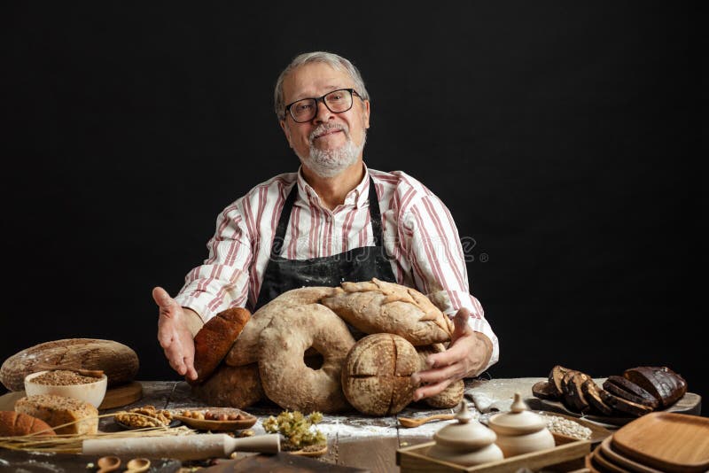 Vieux boulanger heureux regardant la cam?ra et souriant tout en ?treignant des miches de pain