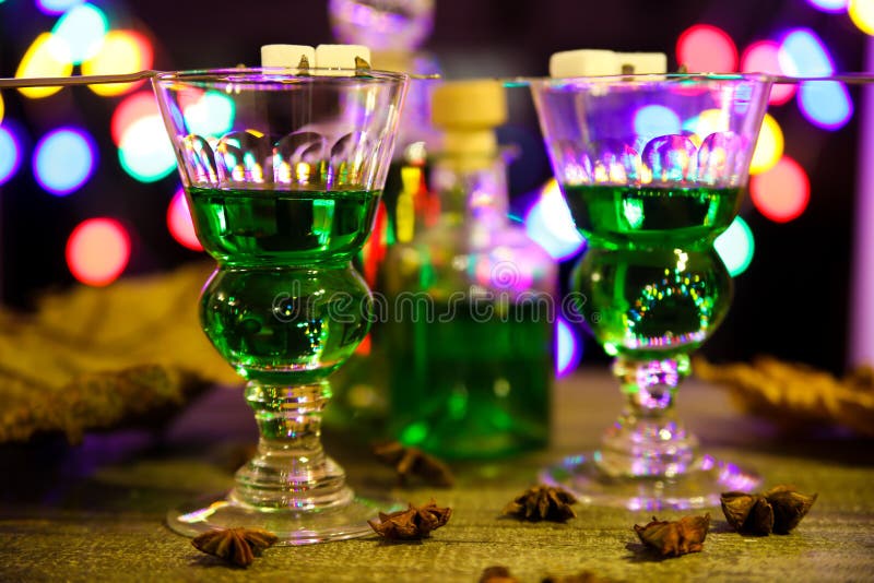 View on alcohol glasses and bottle with green absinthe drink, colorful vibrant bright bokeh background -  binge coma drinking