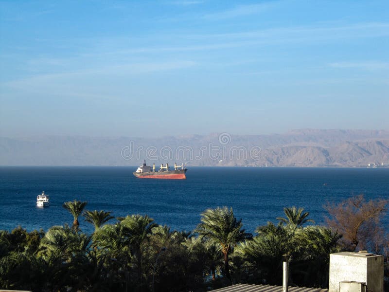 View from the balcony to the sea Bay where a huge cargo ship can be seen through the palm trees royalty free stock photography View from the balcony to the sea Bay where a huge cargo ship can be seen through the palm trees royalty free stock photography