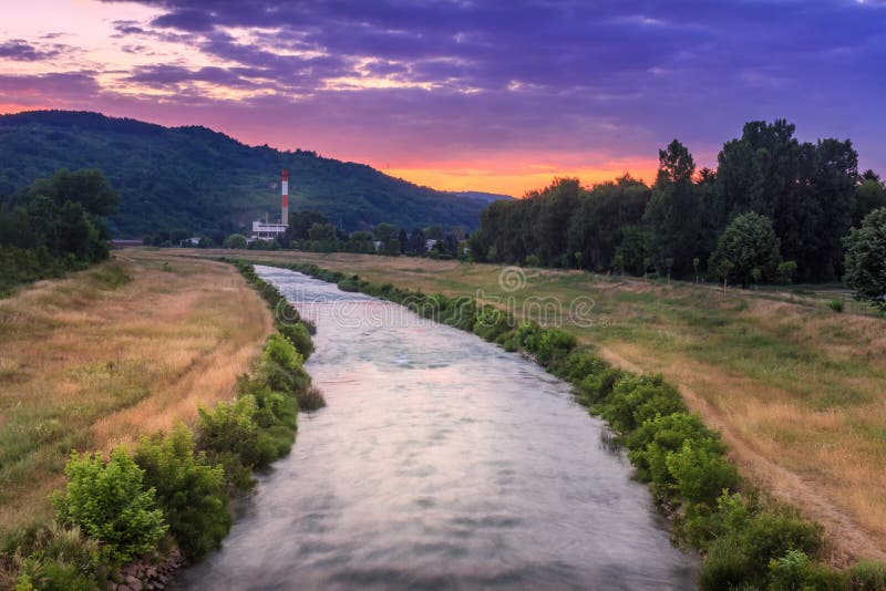 View of blurred motion Nisava river and old factory during vivid, colorful sunset