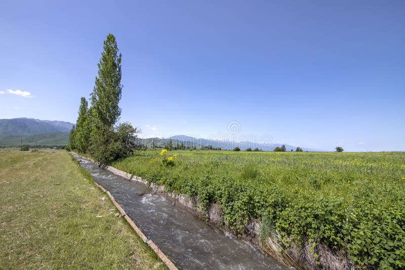 View of the central Tien Shan mountains in Kyrgyzstan with flowing water in the aryk and green fields royalty free stock photography View of the central Tien Shan mountains in Kyrgyzstan with flowing water in the aryk and green fields royalty free stock photography