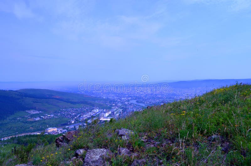 View of the city of Chita. From a height you can see hills covered with forest, a river, city quarters, sky, haze above the city.