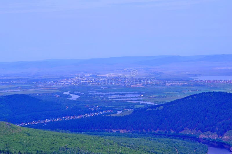 View of the city of Chita. From a height you can see hills covered with forest, a river, city quarters, sky, haze above the city.