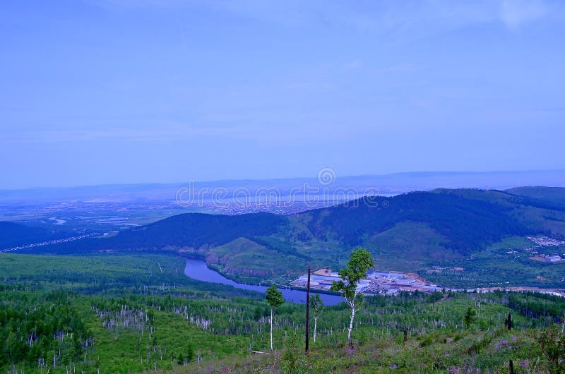 View of the city of Chita. From a height you can see hills covered with forest, a river, city quarters, sky, haze above the city.