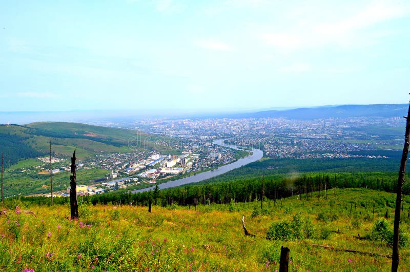 View of the city of Chita. From a height you can see hills covered with forest, a river, city quarters, sky, haze above the city.