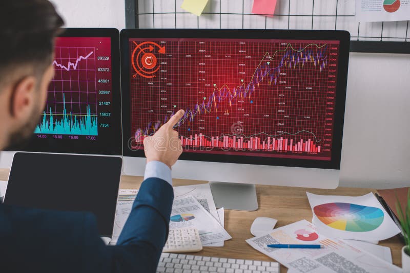 View of data analyst pointing on charts on computer monitor near laptop with blank screen on table stock photos