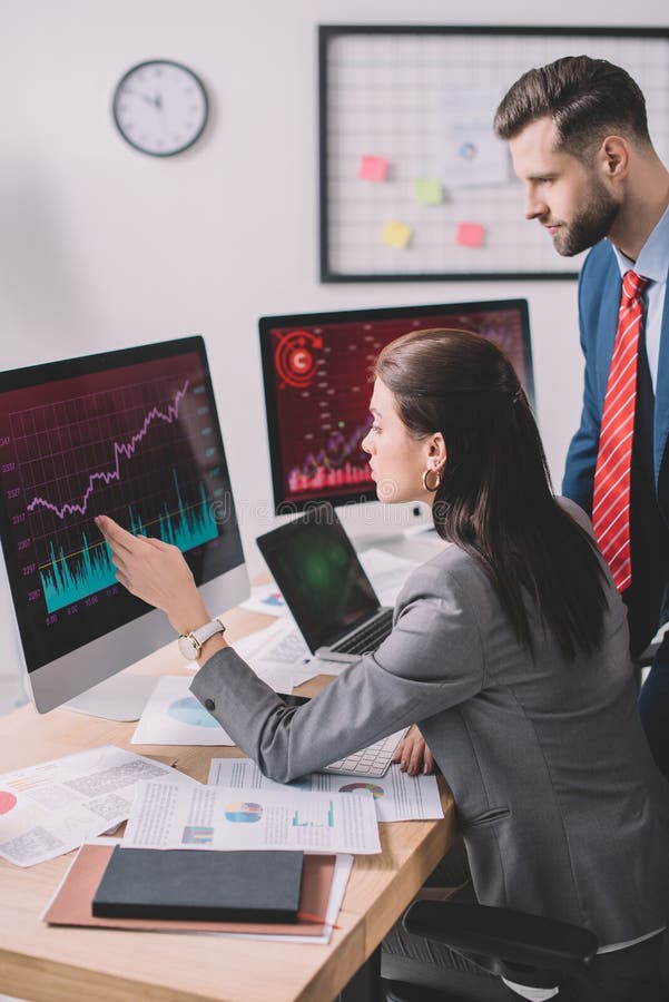 View of data analyst pointing with hand at graphs on computer monitor to colleague in office royalty free stock photos
