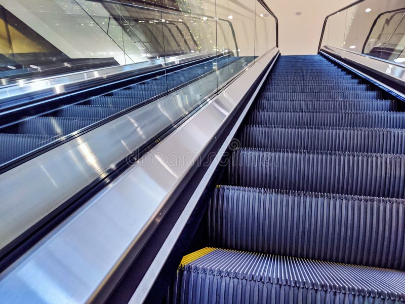 View of empty, yellow lined escalator steps inside a building, leading up to another level