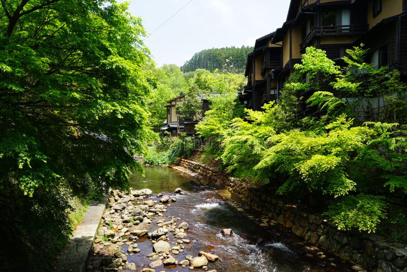 View of fresh stream with stone bank through green trees and local buildings on stone bank in Kurokawa onsen town royalty free stock photo View of fresh stream with stone bank through green trees and local buildings on stone bank in Kurokawa onsen town royalty free stock photo