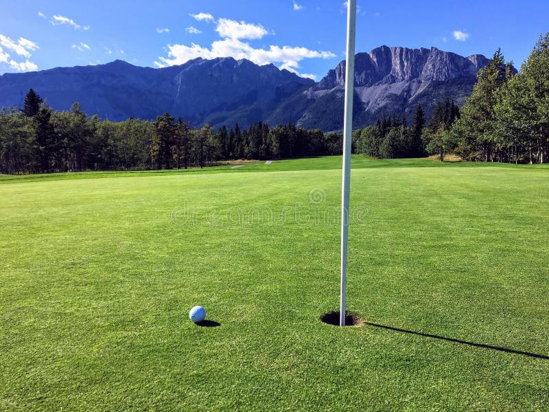 A view of a golf ball on a green close to the hole with the mountains and forest in the background on a beautiful summer day. royalty free stock image A view of a golf ball on a green close to the hole with the mountains and forest in the background on a beautiful summer day. royalty free stock image