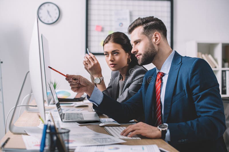 View of information security analyst pointing at computer monitor to colleague in office stock image