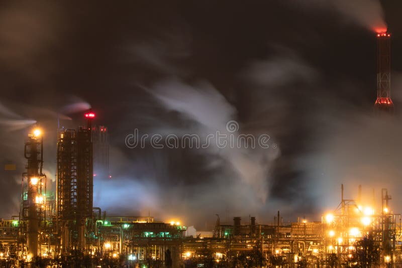 View of a large factory or plant in the light of night lighting. A lot of smoke comes out of the factory\ s chimneys.