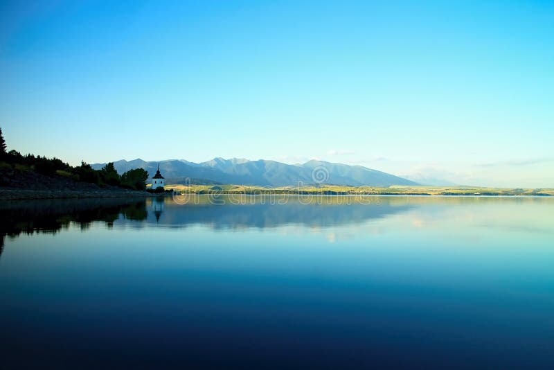 View on level water in dam Liptovska Mara with the background of the Havranok church and West Tatras mountains. Beautiful Slovak s