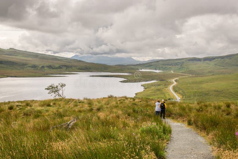 A view from the new and easier path on the Storr. Glamaig mountain in the distance shrouded in clouds. two tourists enjoying the stock photography A view from the new and easier path on the Storr. Glamaig mountain in the distance shrouded in clouds. two tourists enjoying the stock photography