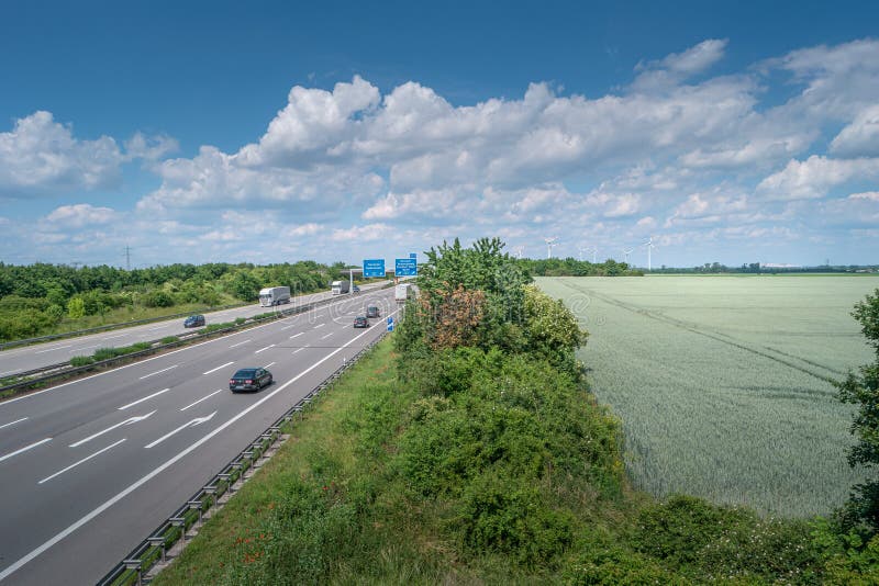 View over beautiful green farm landscape Germany with clouds in sky, wind turbines to generate electrical power and highway with