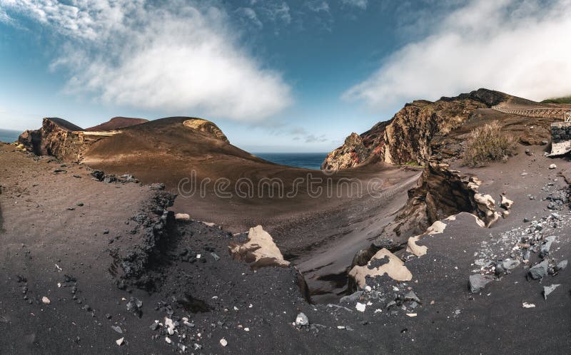 View over Capelinhos volcano, lighthouse of Ponta dos Capelinhos on western coast on Faial island, Azores, Portugal on a sunny day with blue sky and clouds and waves. Last volcano eruption was in 1957. Photo taken in Azores, Portugal.