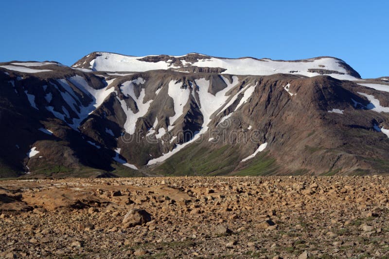 View over stony barren ground on Mountain partly covered with snow and ice contrasting with cloudless blue sky, Iceland stock images View over stony barren ground on Mountain partly covered with snow and ice contrasting with cloudless blue sky, Iceland stock images