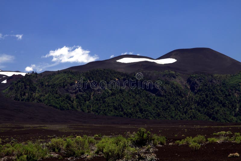View over wide field of volcanic lava ash on peak of black Volcano Llaima with spots and stripes of snow and ice stock images View over wide field of volcanic lava ash on peak of black Volcano Llaima with spots and stripes of snow and ice stock images