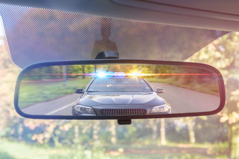 View on rear mirror of a car. Police car with lights and siren is chasing you