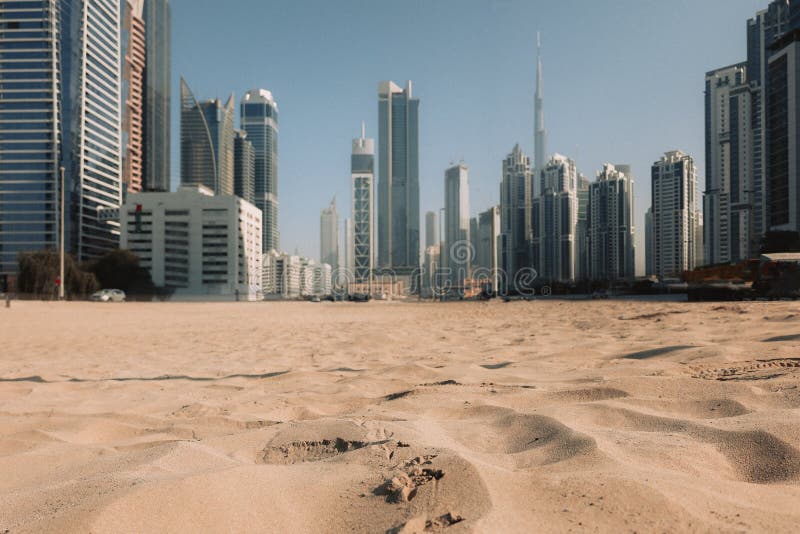 View of sand dunes of desert against backdrop of blurry skyscrapers. Financial business part of city, Dubai, United Arab