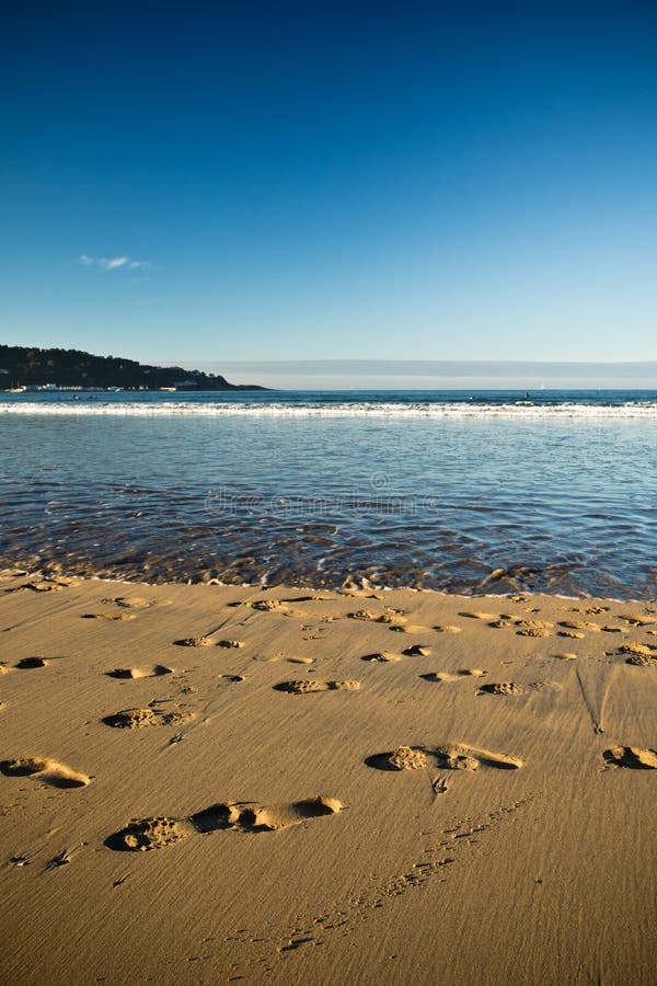 View on sandy beach with feet traces and atlantic ocean with blue sky in sunset