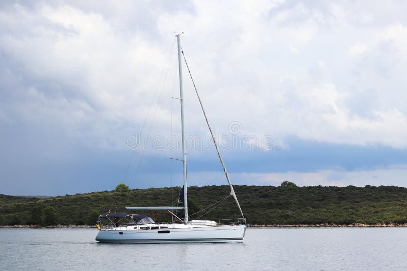 View from the side to the sailing yacht going under the motor past the green shore against the sky with storm clouds. Active rest royalty free stock photo View from the side to the sailing yacht going under the motor past the green shore against the sky with storm clouds. Active rest royalty free stock photo