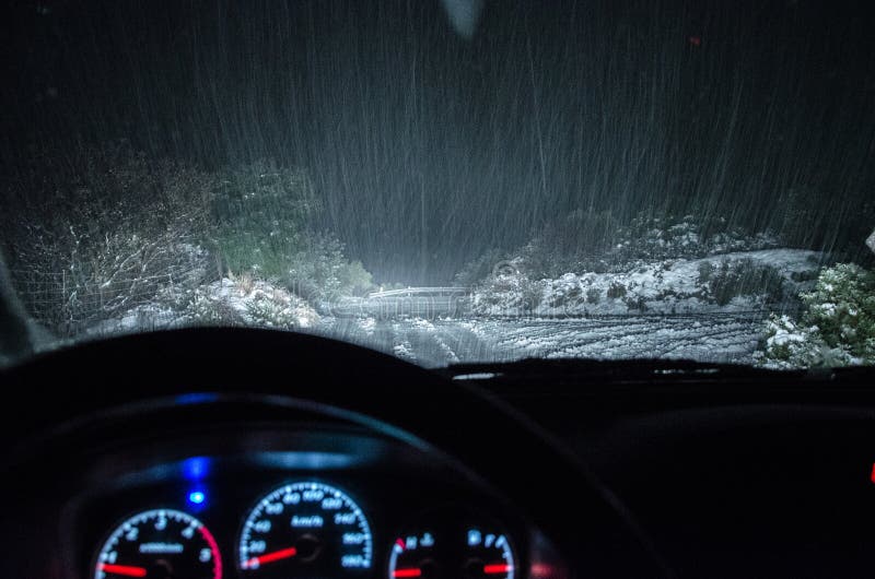 View of snowfall from the car`s windshield at narrow country road at night.