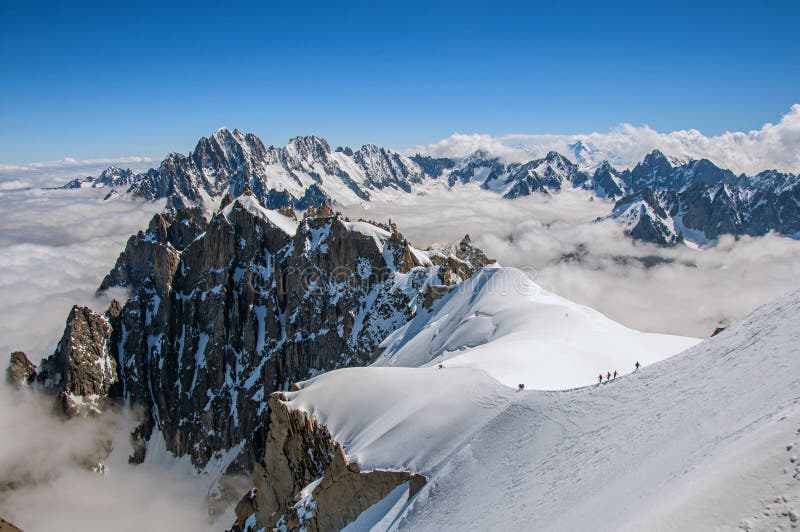 View of snowy peaks and mountaineers from the Aiguille du Midi, in French Alps Chamonix Mont Blanc, alpine mountains landscape, clear blue sky in warm sunny summer day. View of snowy peaks and mountaineers from the Aiguille du Midi, in French Alps Chamonix Mont Blanc, alpine mountains landscape, clear blue sky in warm sunny summer day