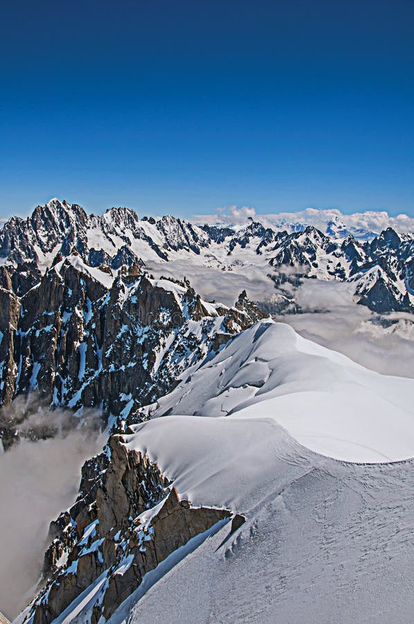 View of snowy peaks and mountaineers from the Aiguille du Midi, in French Alps Chamonix Mont Blanc, alpine mountains landscape, clear blue sky in warm sunny summer day. Retouched photo. View of snowy peaks and mountaineers from the Aiguille du Midi, in French Alps Chamonix Mont Blanc, alpine mountains landscape, clear blue sky in warm sunny summer day. Retouched photo