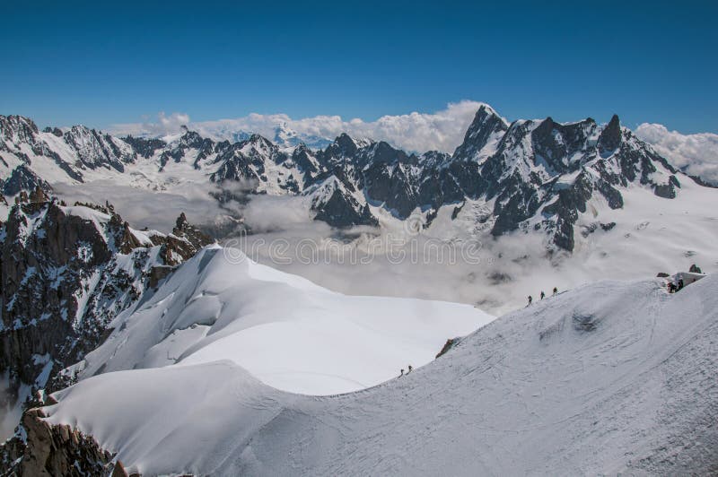 View of snowy peaks and mountaineers from the Aiguille du Midi, in French Alps Chamonix Mont Blanc, alpine mountains landscape, clear blue sky in warm sunny summer day. Retouched photo. View of snowy peaks and mountaineers from the Aiguille du Midi, in French Alps Chamonix Mont Blanc, alpine mountains landscape, clear blue sky in warm sunny summer day. Retouched photo