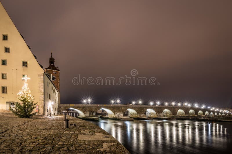 View to the stone bridge in Regensburg at night in fog over the river Danube with illuminated Christmas tree, Germany 2020