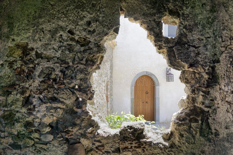 View on a wooden door of a new house through the opening in the wall of an old ruined building