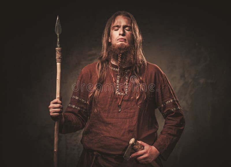 Vikingo serio con una lanza en un guerrero tradicional viste, presentando en un fondo oscuro fotografía de archivo Vikingo serio con una lanza en un guerrero tradicional viste, presentando en un fondo oscuro fotografía de archivo