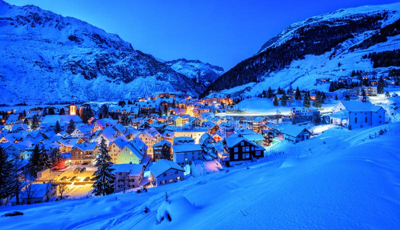 Vila de Andermatt em montanhas dos cumes na neve do inverno, Uri, Suíça