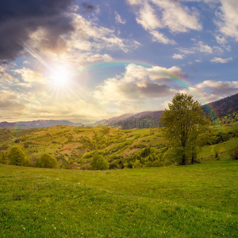 Villaggio sul prato del pendio di collina in montagna al tramonto dell'arcobaleno fotografia stock Villaggio sul prato del pendio di collina in montagna al tramonto dell'arcobaleno fotografia stock