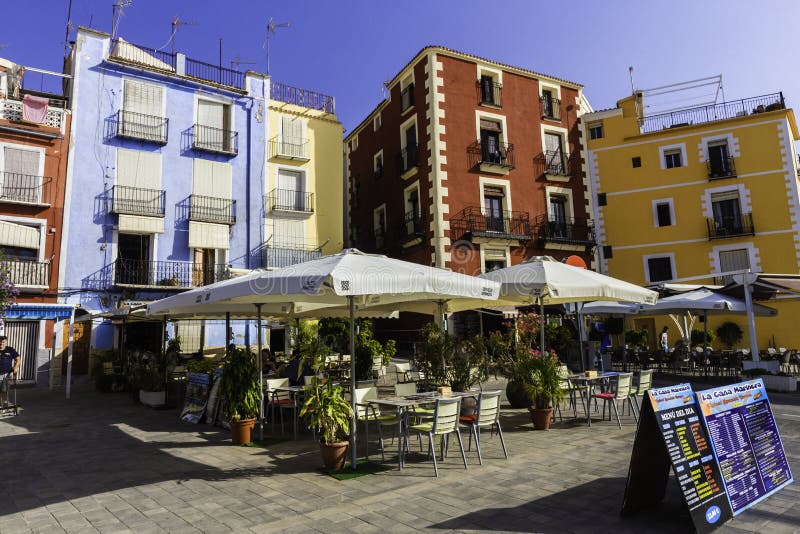 Villajoyosa, Spain - July 3, 2018: Cafe, colorful houses and palms on the street in Villajoyosa on a sunny day. Villajoyosa, Spain - July 3, 2018: Cafe, colorful houses and palms on the street in Villajoyosa on a sunny day.