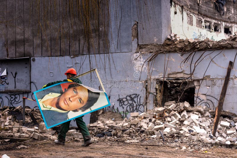 Vilnius, Lithuania- March 03, 2017:. Worker is carrying metal frame with poster of Alain Delon in background of being demolished former cinema theatre “Lietuva” (built in 1965 in Lithuanian republic of Soviet Union), closed in 2022, in Independent Lithuania. Vilnius, Lithuania- March 03, 2017:. Worker is carrying metal frame with poster of Alain Delon in background of being demolished former cinema theatre “Lietuva” (built in 1965 in Lithuanian republic of Soviet Union), closed in 2022, in Independent Lithuania.