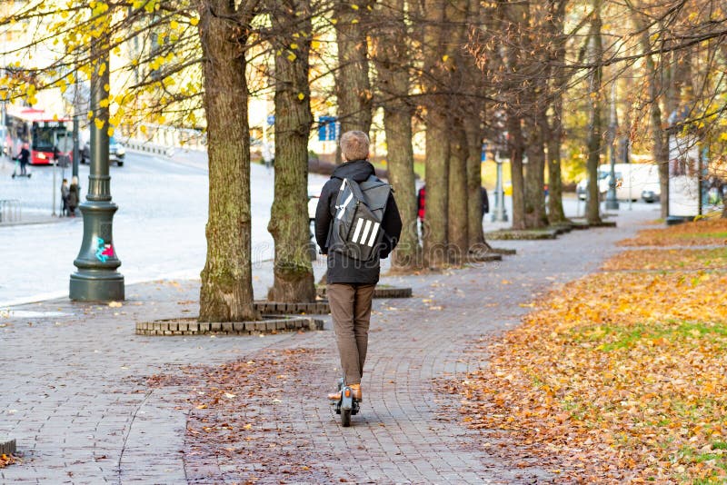 Vilnius, Lithuania - November 6 2020: Boy with electric scooter and backpack. Sustainable transport. Road bike with trees and autumn background