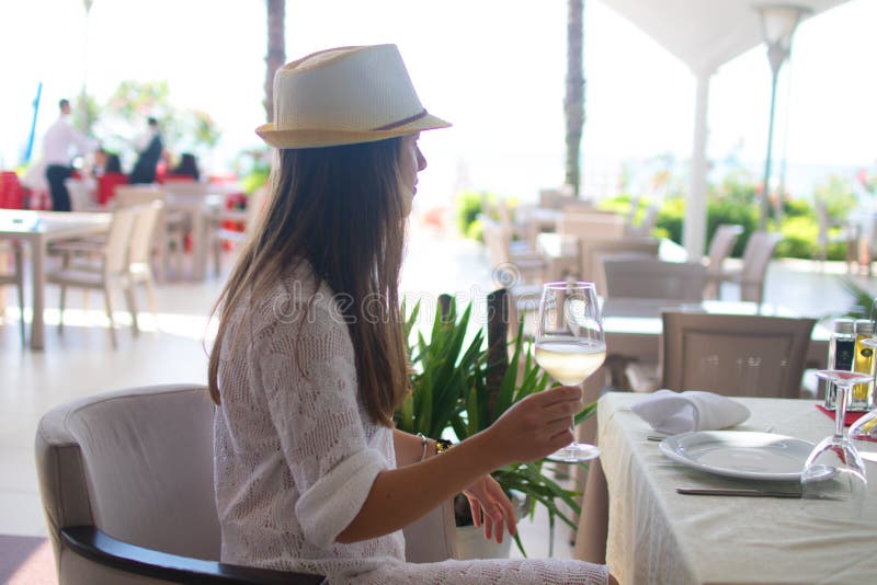 Vin blanc potable de jeune femme sur la terrasse extérieure observant dessus de la mer Méditerranée Femelle dans le bain de solei images stock Vin blanc potable de jeune femme sur la terrasse extérieure observant dessus de la mer Méditerranée Femelle dans le bain de solei images stock