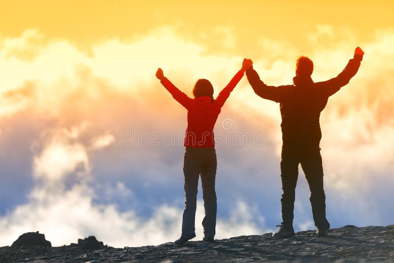 Happy winners reaching life goal - success people at summit. Business achievement concept. Two person couple together arms up in the air of happiness with accomplishment in the clouds at sunset. Happy winners reaching life goal - success people at summit. Business achievement concept. Two person couple together arms up in the air of happiness with accomplishment in the clouds at sunset.