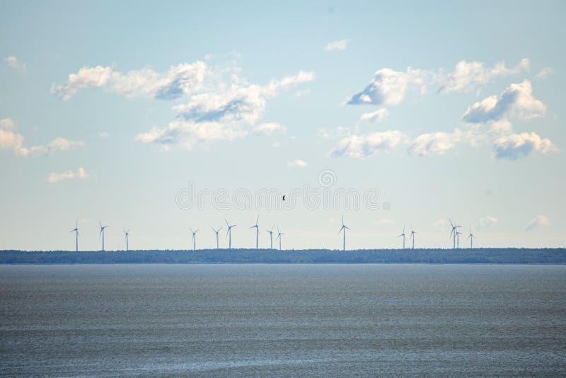 Vindkvarnar vid horisonten med moln i klart himmel och hav i förgrunden Vindturbiner, vindkraftparker som producerar elkraft. arkivbilder Vindkvarnar vid horisonten med moln i klart himmel och hav i förgrunden Vindturbiner, vindkraftparker som producerar elkraft. arkivbilder