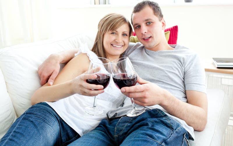 Vinho bebendo dos pares novos bonitos no sofá fotografia de stock Vinho bebendo dos pares novos bonitos no sofá fotografia de stock